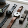 A diverse collection of top-rated smartwatches and fitness trackers for 2026, including rugged circular, sleek minimalist, hybrid analog, and fabric strap designs, laid out on a wooden desk.