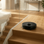 A modern black robot vacuum cleaner positioned safely at the top of a wooden staircase in a bright multi-level home.