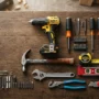 Professional-grade home hardware tools including a cordless drill, forged steel hammer, and multi-bit screwdriver set arranged on a wood workbench for a home toolkit.