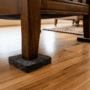 Close-up of heavy wooden furniture legs sitting on thick dark grey felt floor protectors on a polished light hardwood timber floor to prevent scratches and scuffs.