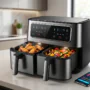 Air Fryers With Dual-Zone Sync -A modern black smart air fryer with dual-zone sync capability, simultaneously cooking crispy chicken wings in one basket and roasted vegetables in the other, next to a smartphone displaying the control app on a kitchen counter.