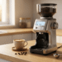 A premium stainless steel smart coffee grinder with a digital display sitting next to a glass of freshly brewed coffee on a modern kitchen counter.